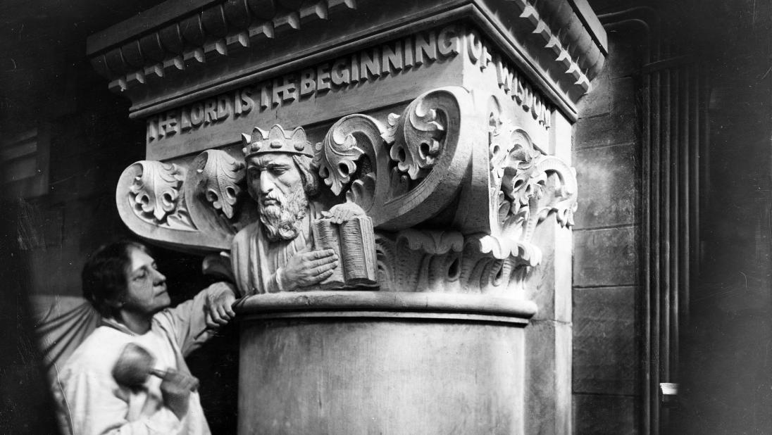 A woman stands beneath a carving of King Solomon, a Biblical figure, holding her chisel.