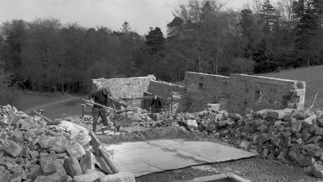 A man stands in the middle of a house being built. The nearby stones are numbered.