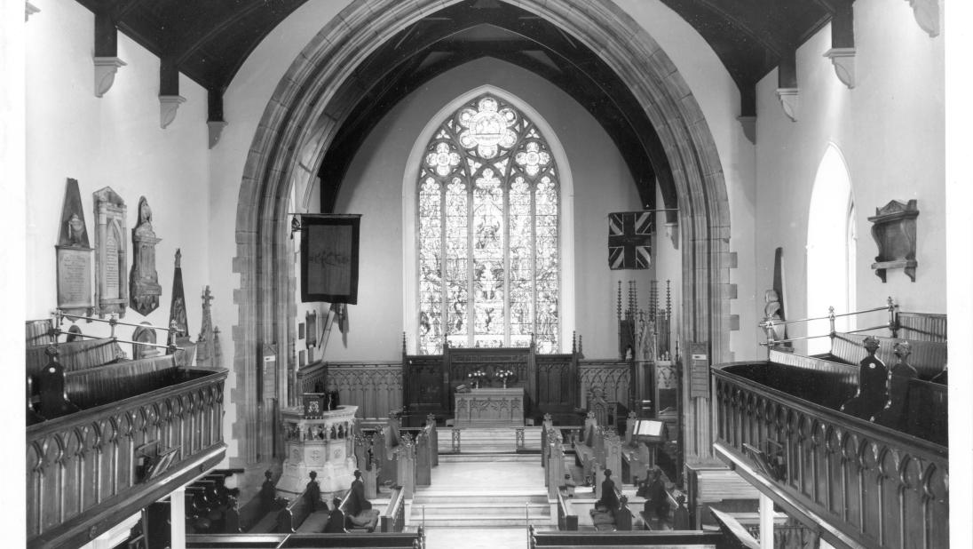 A wide shot of a church interior, with a focus on the stained glass window in the background.