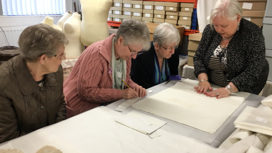 A group of women sit around a table discussing textiles. 
