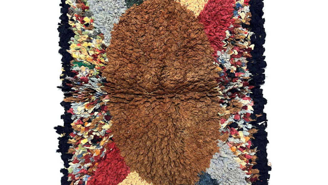 A colourful rug with a golden oval centre. Two red and yellow and two blue and green triangles eminate from the oval. It has a black edge.