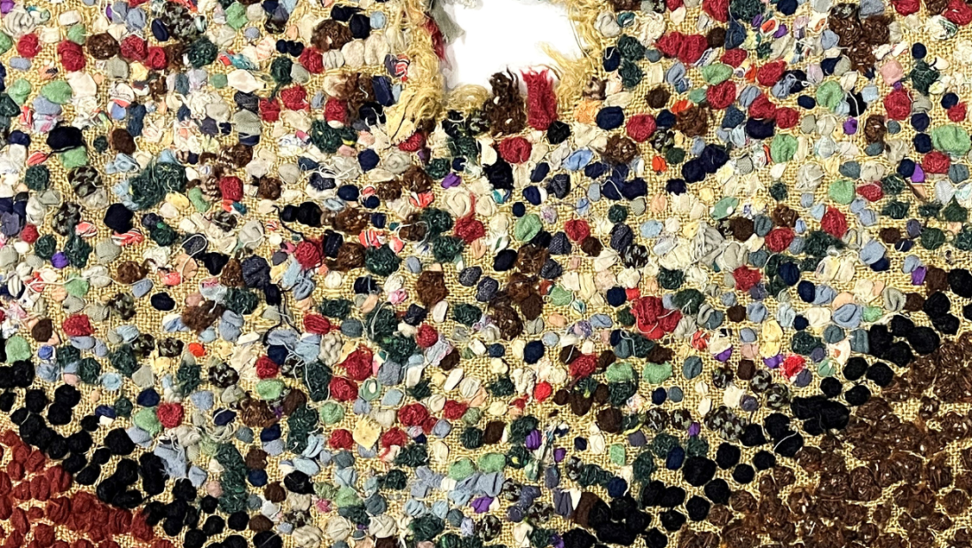 A detail shot of a rug. We can see a multicolour section with a hole. The outer sections are brown and red..