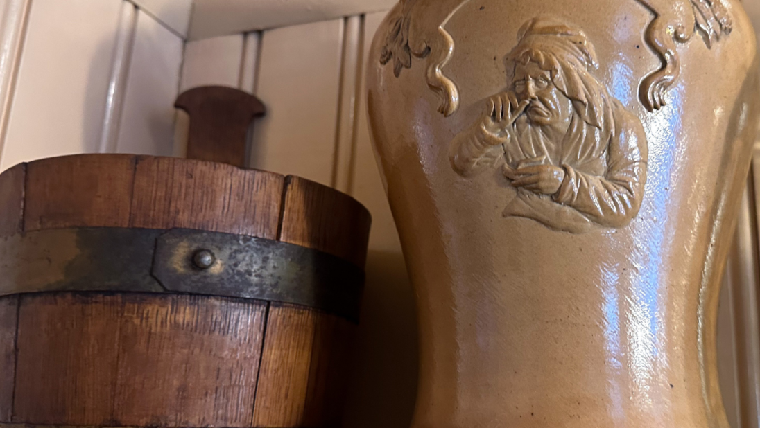 A noggin and a jar for tobacco sit on a shelf.