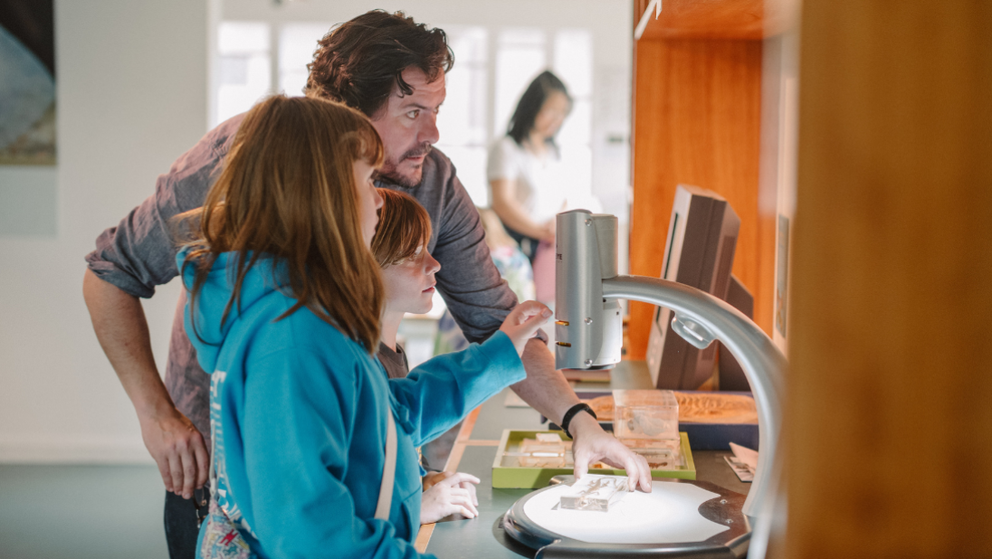 a man and two children looking in a microscope in discover nature