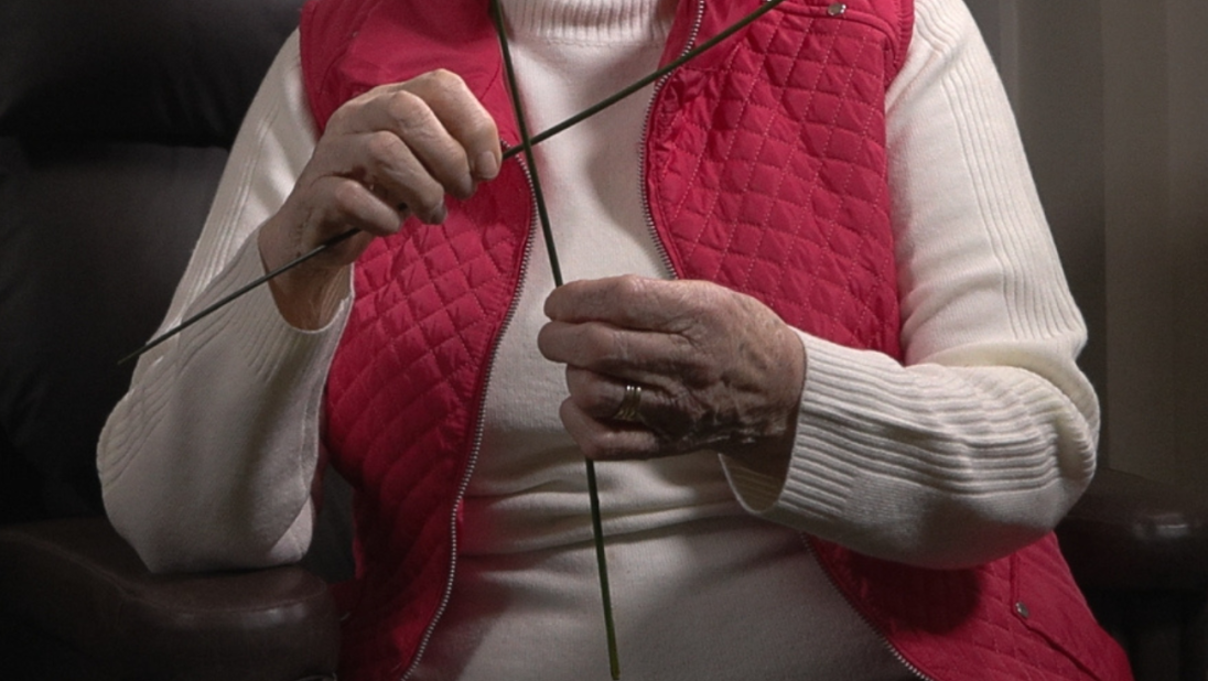 A woman in a red cardigan weaves a St. Brigid's Cross.