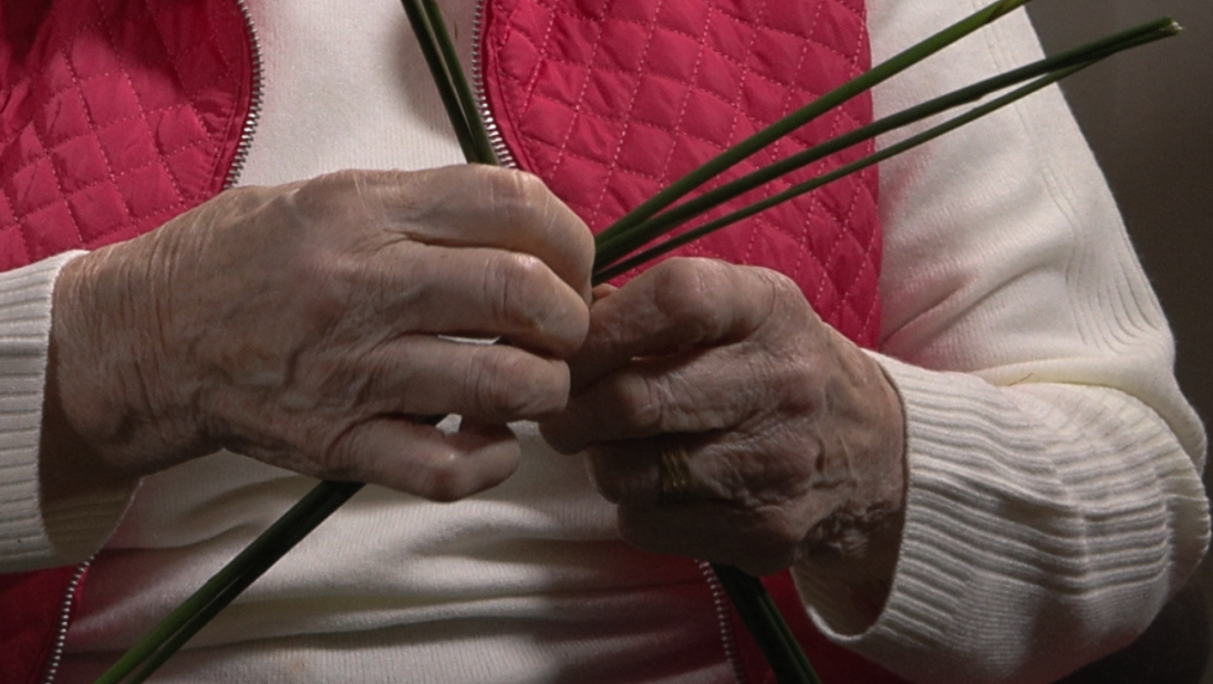 A woman in a red cardigan weaves a St. Brigid's Cross.