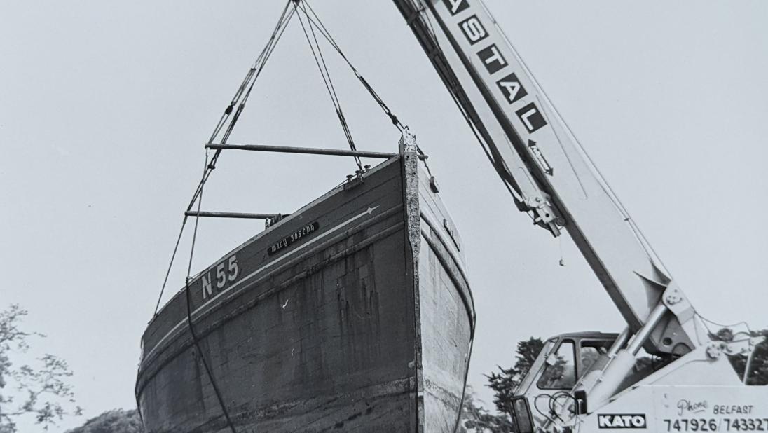 Black and white photograph of the Mary Joseph nickey boat being moved by a crane