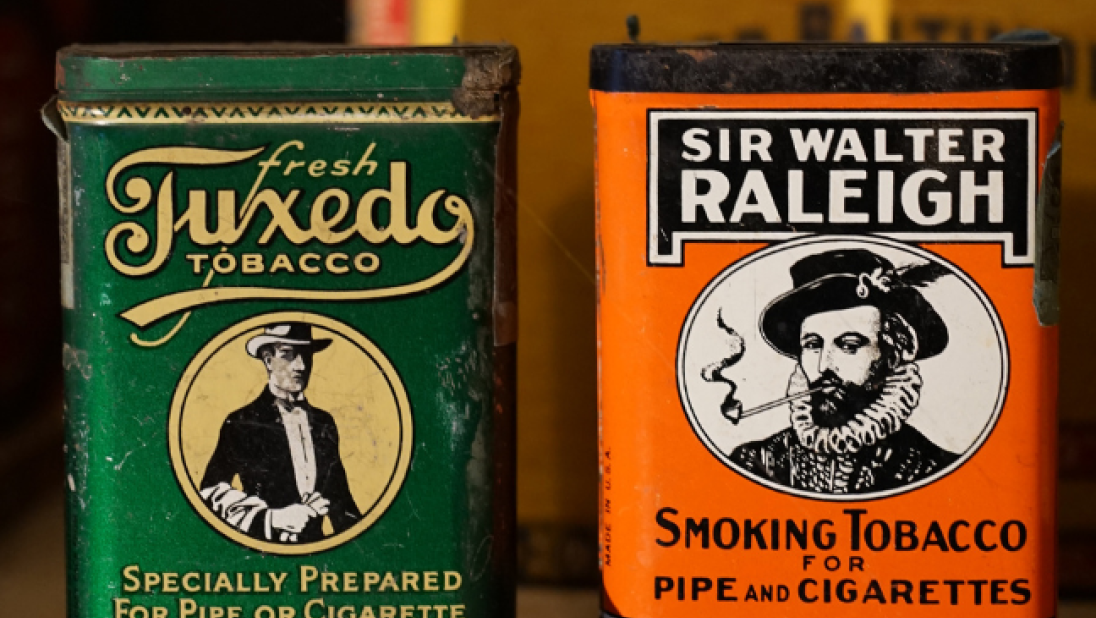 Two tobacco tins sit on a shelf. 