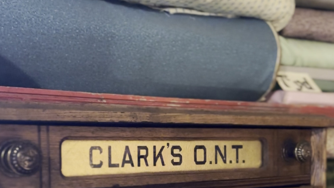 Cotton sheets sit atop one another on a shelf, above a sign reading 'Clark's ONT spool cotton'.