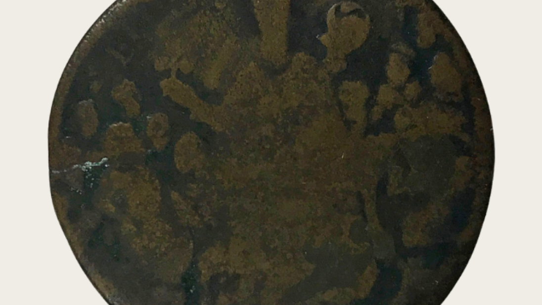 An old, worn coin. An image of St. Patrick holding a three leaf clover is just visible.