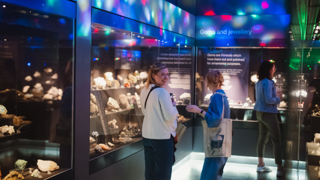 Three people inside a fossil gallery in a museum done up as a cave rave with disco lights for an event.
