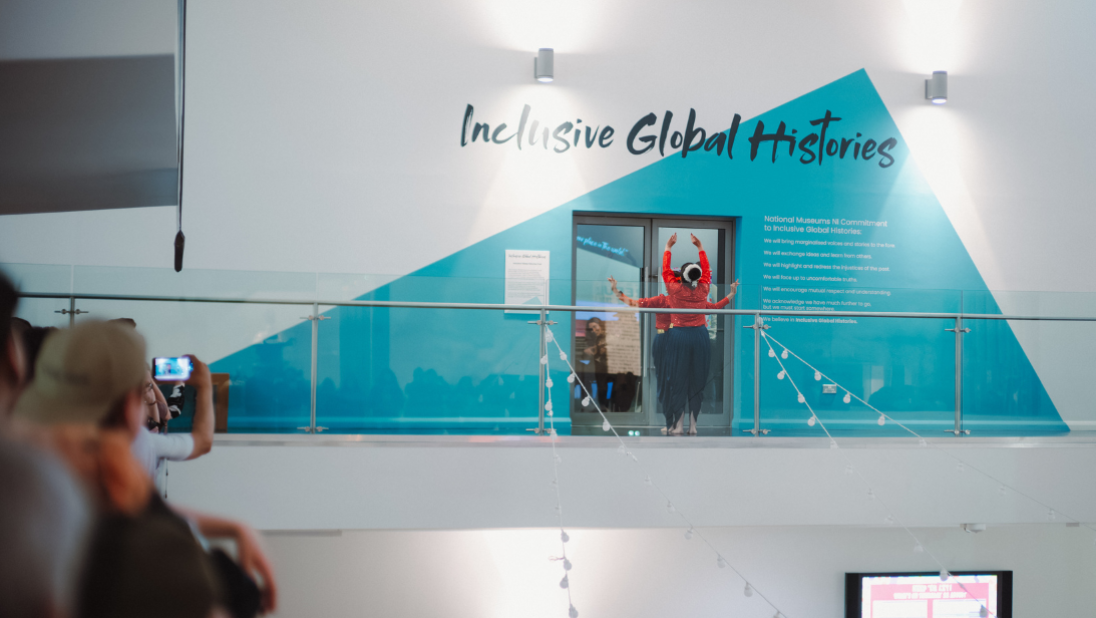Dancers on the hallway of a museum out the front of an exhibition called Inclusive Global Histories. The walls are painted blue and white.