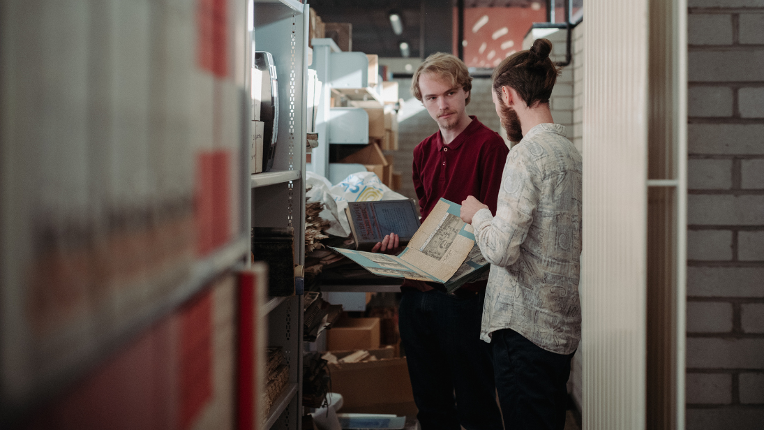 Two young males in a library looking at an open book
