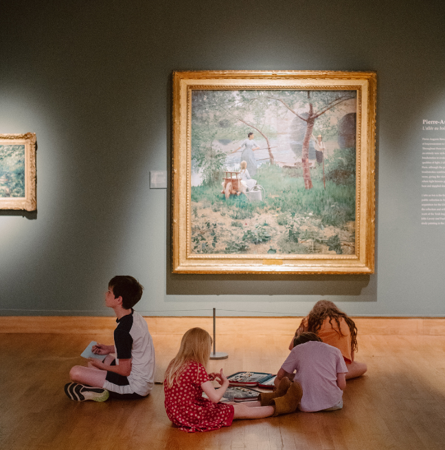 Primary school age kids sitting on the wooden floor of an art gallery in Ulster Museum drawing.