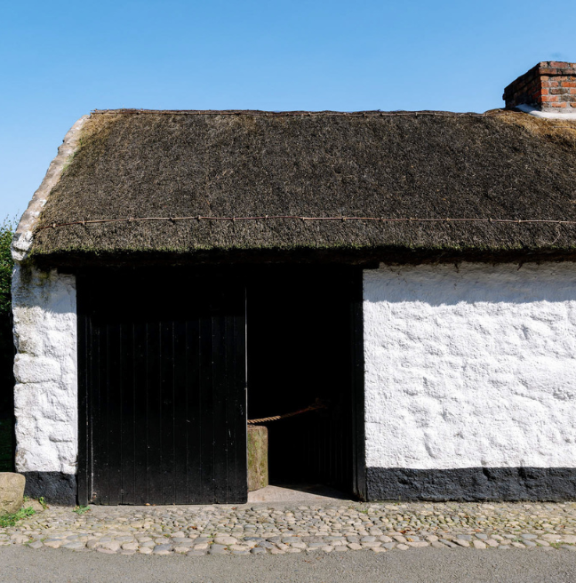 A whitewashed forge sits with its door open, the room inside very dark.