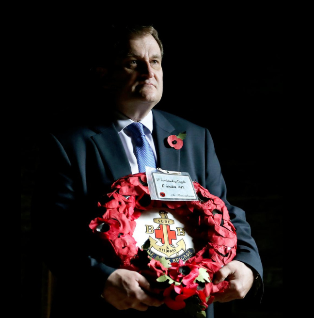 Man in a suit holding a poppy wreath with black background
