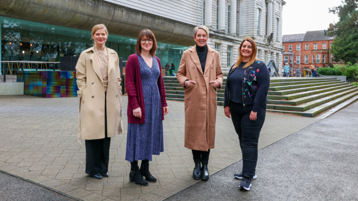 Four women standing out the front of the Ulster Museum, the glass and stone facade in the background.