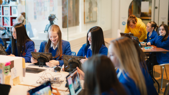 A classroom of girls wearing blue uniforms, sitting with iPads, taking part in a class.