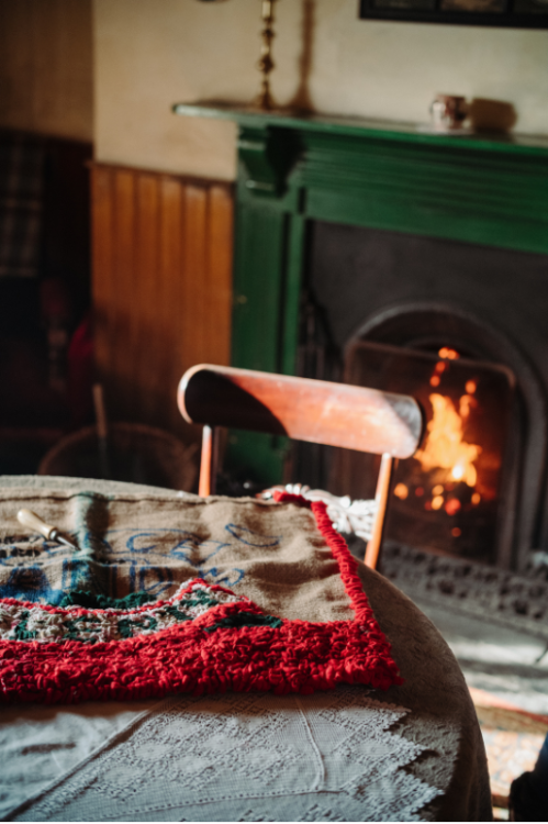 Fire lit with table and chair in view and art on display above fireplace