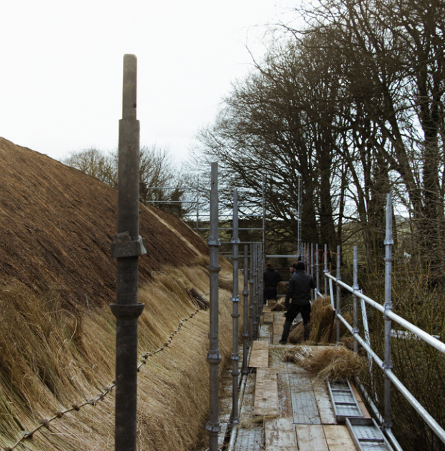 A view of a roof being thatched from up close on scaffolding.