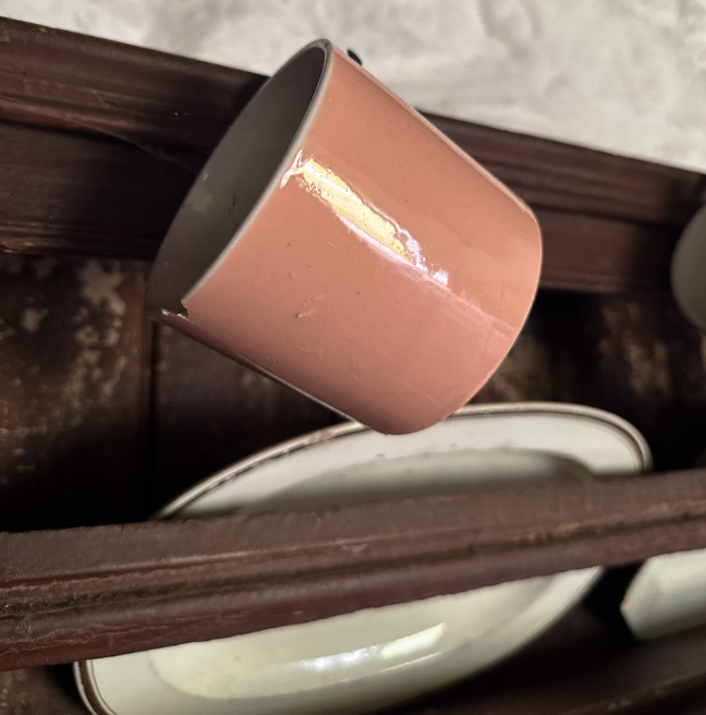 A close up of a pinkish mug hanging on a dresser. The mug has a chip in it.