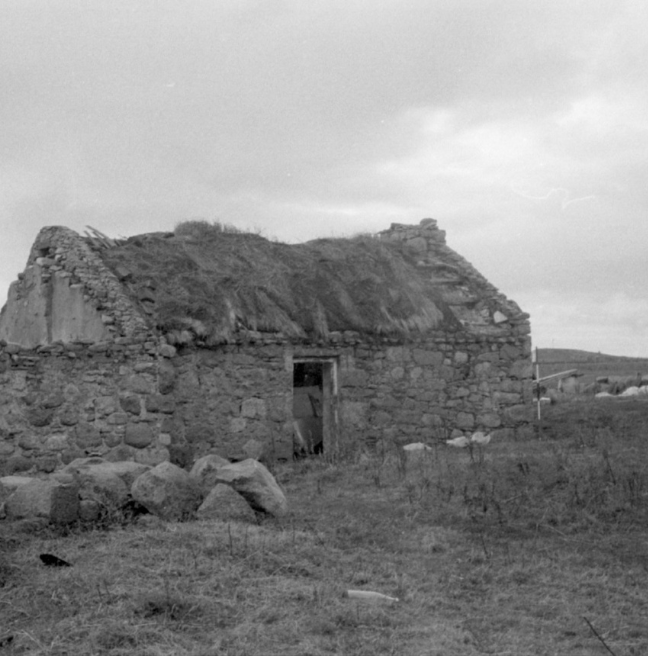 A black and white image of a derelict cottage with a thatched roof falling in and no door.