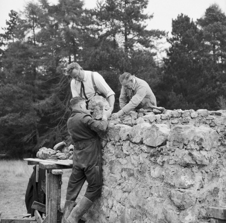 Three men are rebuilding a stone wall of a house.