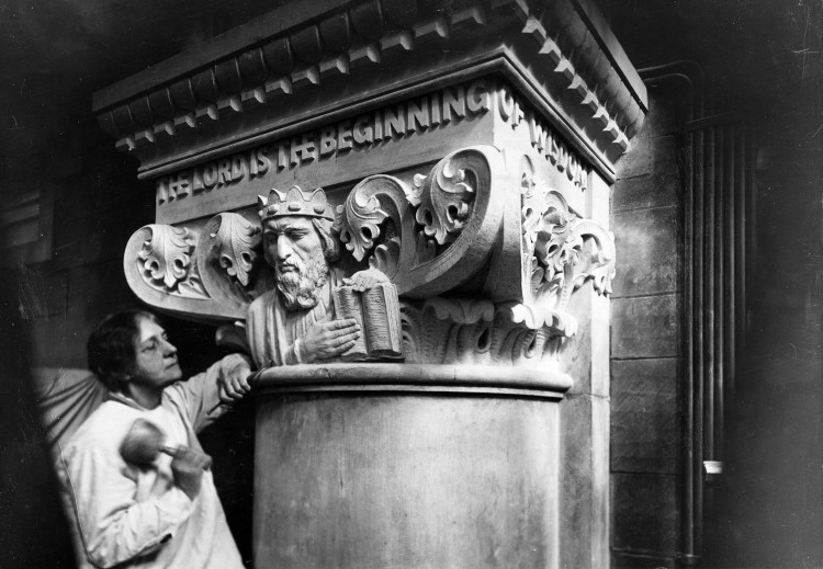 A woman stands beneath a carving of King Solomon, a Biblical figure, holding her chisel.