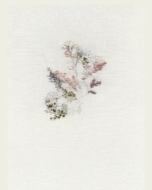 On natural linen, pastel threads form a flower-like artwork.
