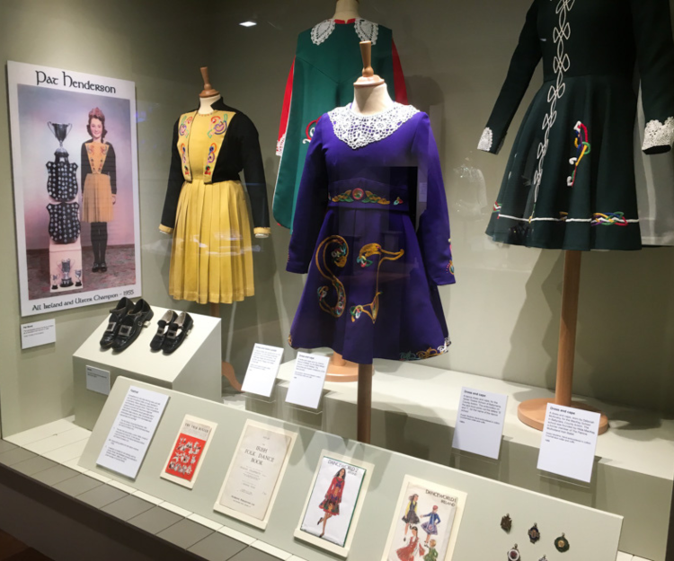 A shot of an exhibition with one yellow, one purple, and one green Irish dancing dress.