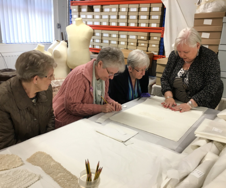 A group of women sit around a table discussing textiles. 