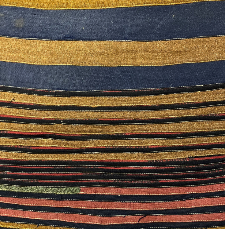 The detail of the back of a rug. It is a striped rug with multiple colours.