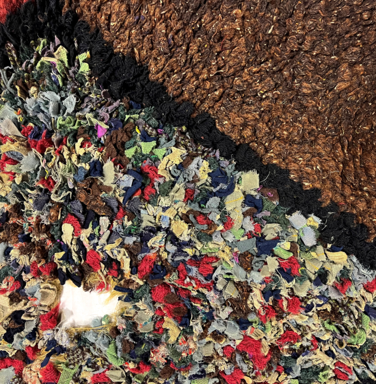A detail shot of a rug. We can see a multicolour section with a hole. The outer section is brown.