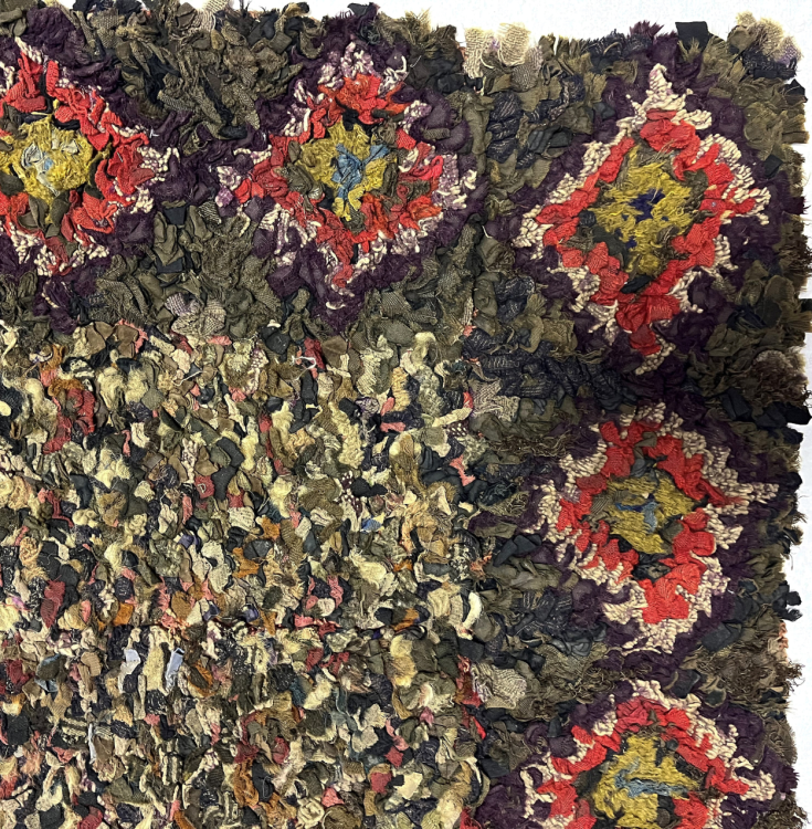 A detailed corner of a rug. The inner rectangle is multicoloured. The outer rectangle has multicoloured diamond shapes decorating the rug every few inches.