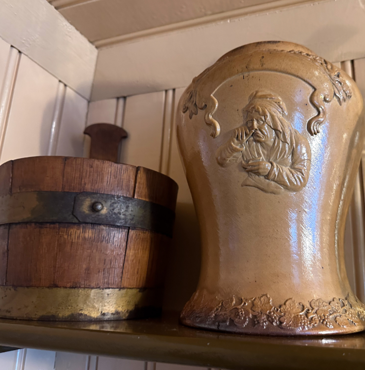 A noggin and a jar for tobacco sit on a shelf.