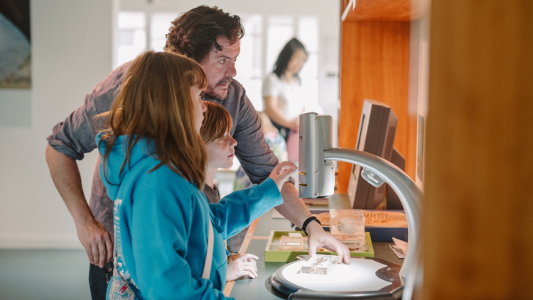 a man and two children looking in a microscope in discover nature