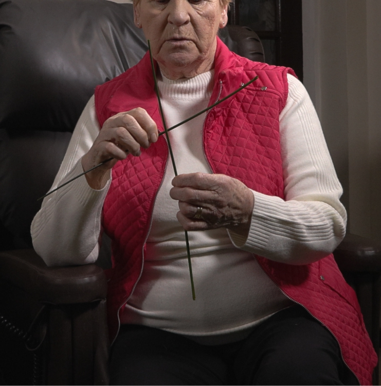 A woman in a red cardigan weaves a St. Brigid's Cross.