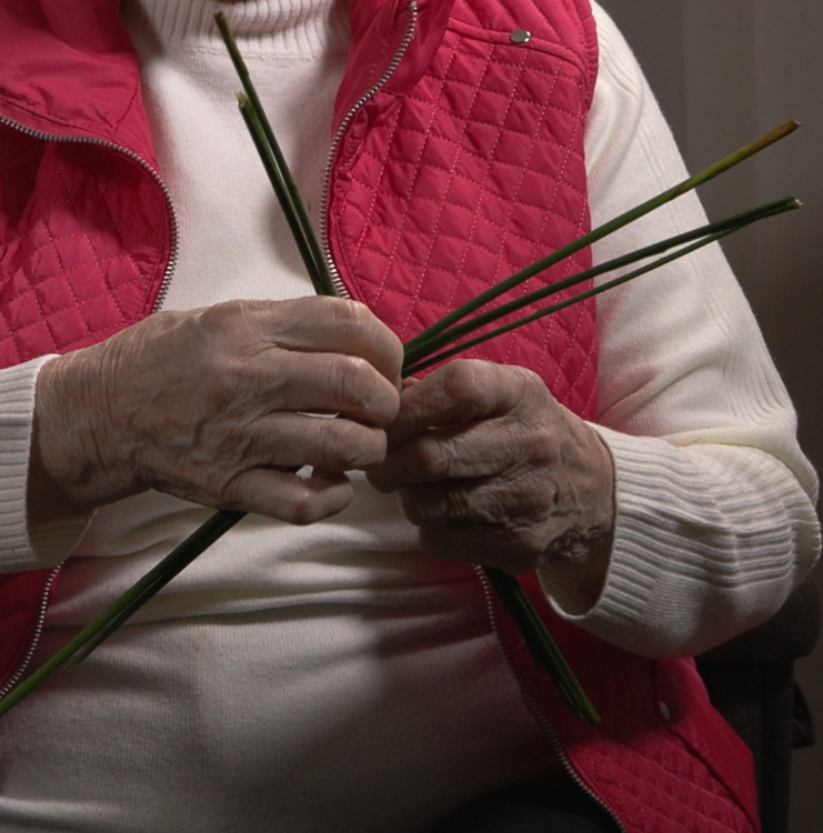 A woman in a red cardigan weaves a St. Brigid's Cross.