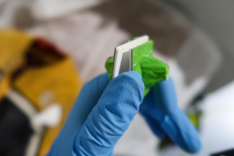 A hand with a blue glove on holds up two small magnets. 