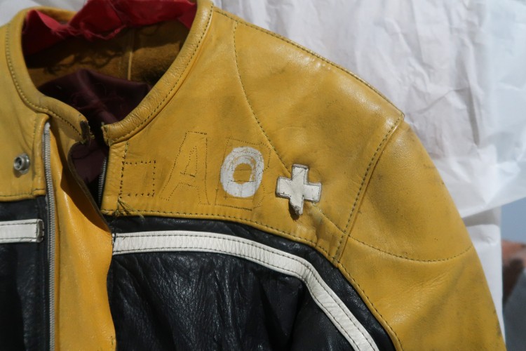 A close up of the top of a racing jumpsuit. There are white patches spelling 'O +' sewn on.