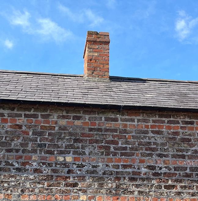 The roof of a vernacular building, where a brick chimney stands restored.