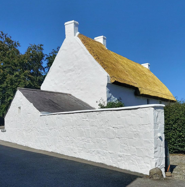 A thatched and whitewashed cottage after a new coat of whitewash stands brightly in the sun.