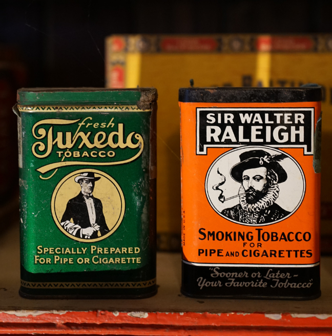 Two tobacco tins sit on a shelf. 