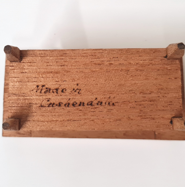 The underside of a wooden table for a basin, for a dolls' house. The words 'Made in Cushendall' are written in cursive. 