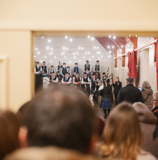 a crowd looking in the door of a room to see the ferguson pipe band