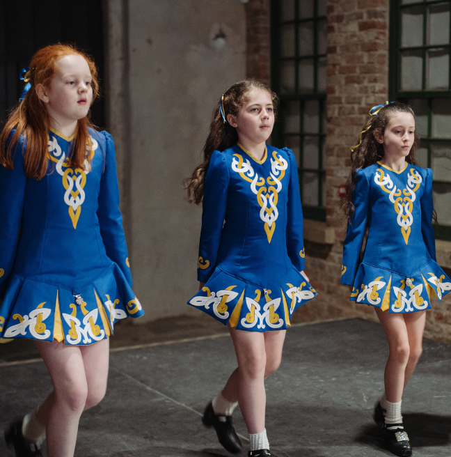 three girls irish dancing in blue traditional costume