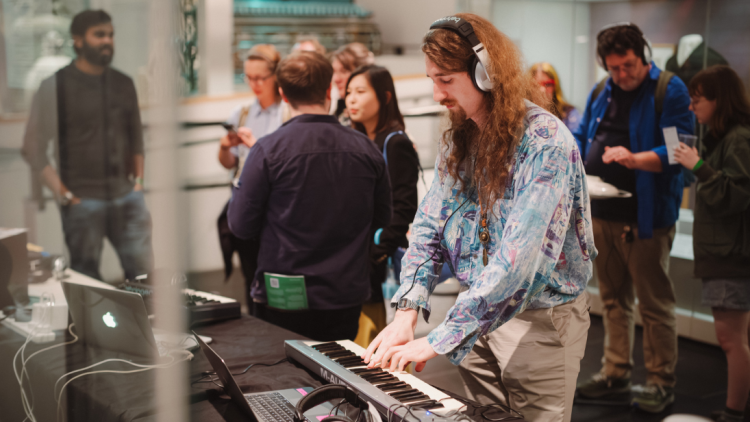 A guy with long, auburn, frizzy hair with headphones on playing a keyvboard.