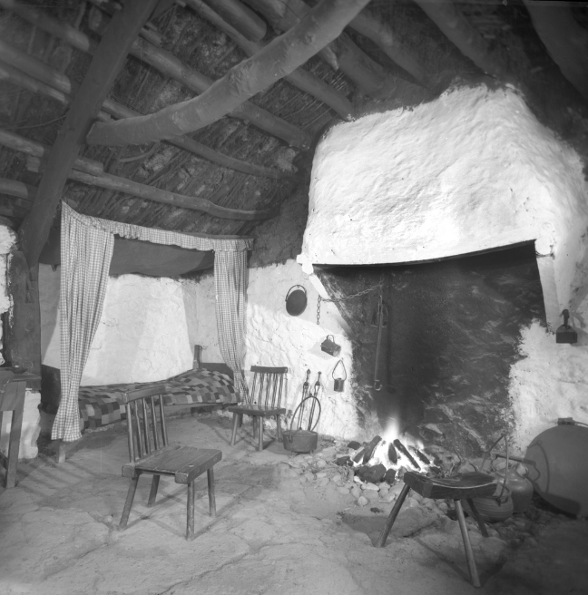 The inside of a cottage showing a large hearth and a bed outshot.