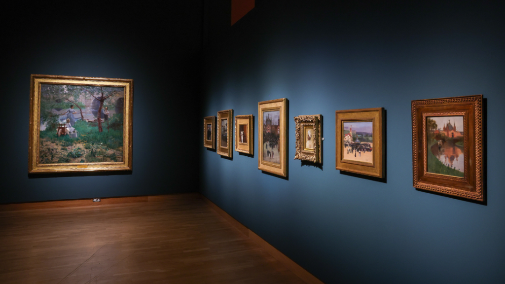 Paintings by Sir John Lavery, hung on a blue painted wall inside a lit up gallery