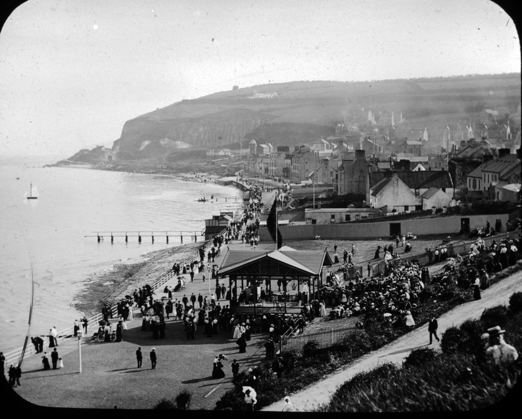 An old black and white image of a seaside town, looking at the beach where festivities are happening.